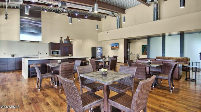 dining room with hardwood / wood-style floors, beamed ceiling, rail lighting, and a towering ceiling