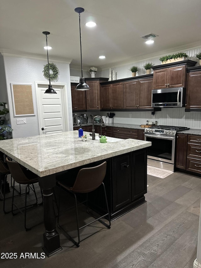 kitchen with a breakfast bar area, a kitchen island with sink, a sink, appliances with stainless steel finishes, and crown molding