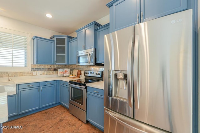 kitchen with tasteful backsplash, blue cabinetry, glass insert cabinets, light countertops, and appliances with stainless steel finishes