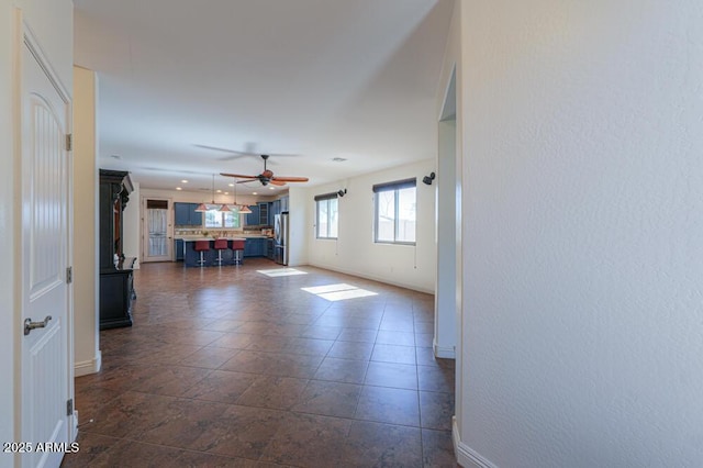 unfurnished living room featuring dark tile patterned floors, a ceiling fan, and baseboards