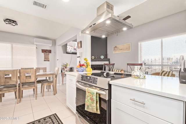 kitchen featuring light tile patterned floors, electric range, a wall mounted AC, island range hood, and white cabinets