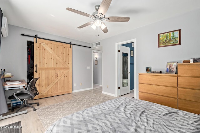 bedroom with ceiling fan, a barn door, ensuite bath, and light hardwood / wood-style flooring