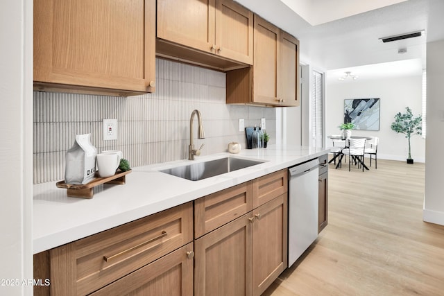 kitchen featuring a sink, backsplash, stainless steel dishwasher, and light countertops