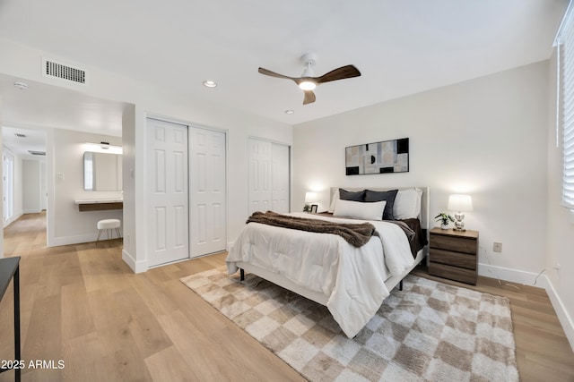bedroom with two closets, baseboards, visible vents, and light wood-type flooring