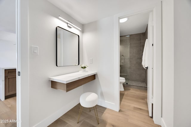 bathroom with toilet, a shower stall, wood finished floors, and baseboards
