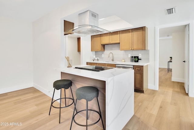 kitchen featuring visible vents, black electric cooktop, a sink, a breakfast bar, and island exhaust hood