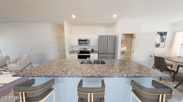 kitchen with a breakfast bar, white cabinetry, sink, light stone counters, and stainless steel appliances