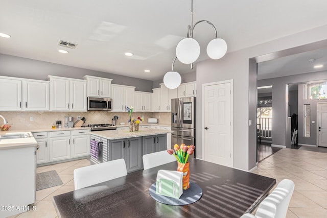 kitchen featuring light tile patterned flooring, white cabinetry, decorative light fixtures, appliances with stainless steel finishes, and a kitchen island