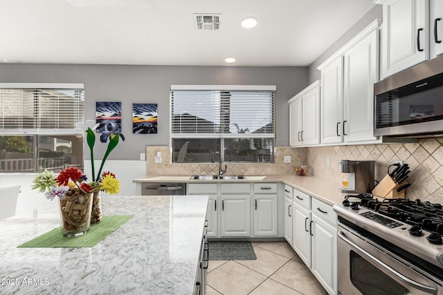 kitchen with light tile patterned flooring, tasteful backsplash, white cabinetry, sink, and stainless steel appliances