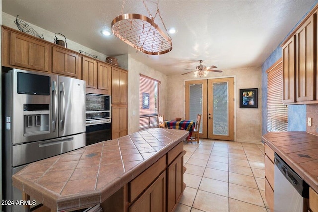 kitchen featuring light tile flooring, ceiling fan, tile countertops, appliances with stainless steel finishes, and french doors