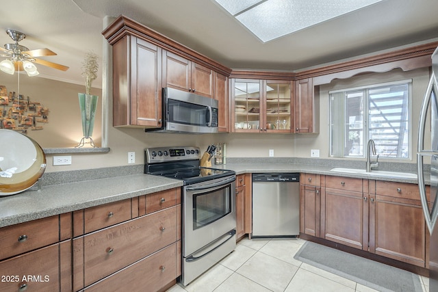 kitchen featuring brown cabinetry, a ceiling fan, a sink, stainless steel appliances, and light tile patterned flooring