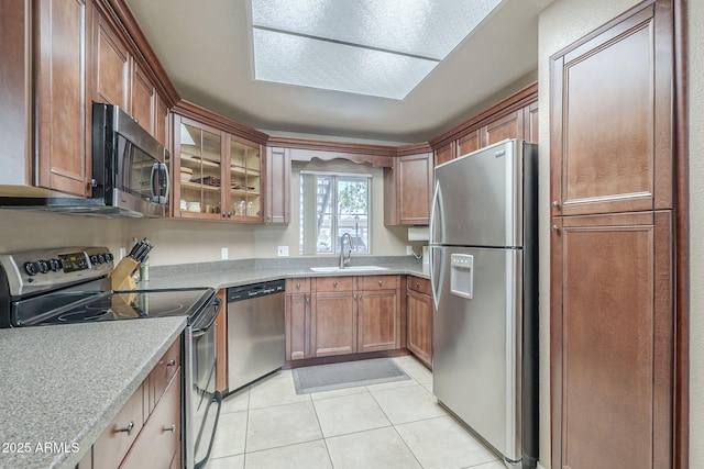 kitchen featuring appliances with stainless steel finishes, a sink, light countertops, light tile patterned floors, and glass insert cabinets