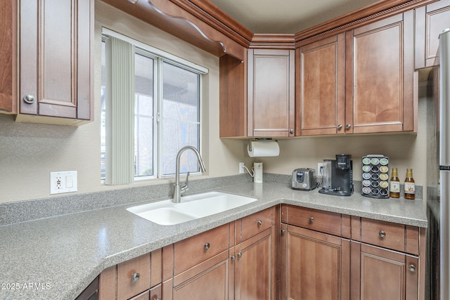 kitchen with light countertops, brown cabinetry, a sink, and freestanding refrigerator