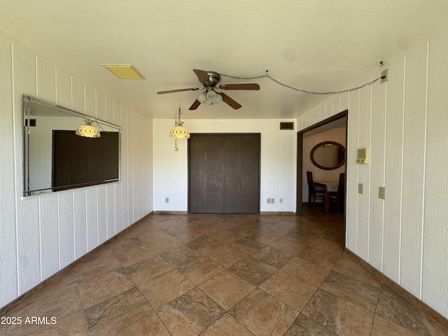 spare room featuring baseboards, ceiling fan, visible vents, and stone finish floor