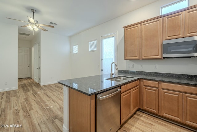 kitchen with kitchen peninsula, stainless steel appliances, sink, light hardwood / wood-style flooring, and dark stone countertops