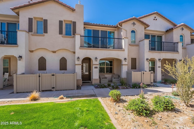 mediterranean / spanish house with a tile roof, a gate, fence, and stucco siding