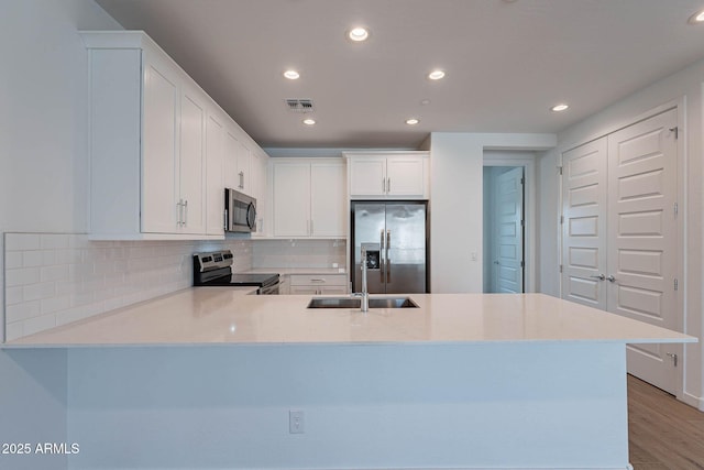 kitchen featuring visible vents, decorative backsplash, appliances with stainless steel finishes, a peninsula, and a sink