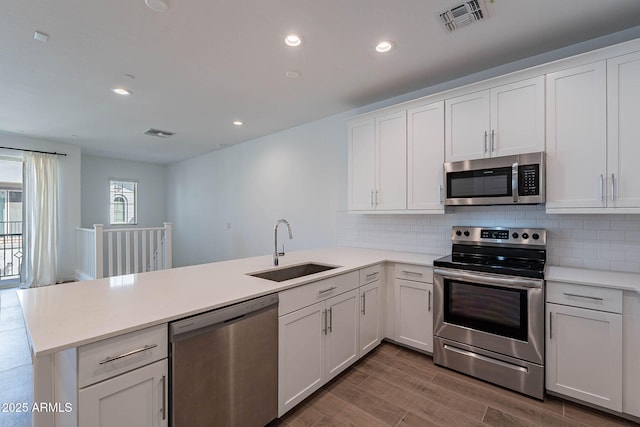 kitchen with a peninsula, wood finished floors, a sink, visible vents, and appliances with stainless steel finishes