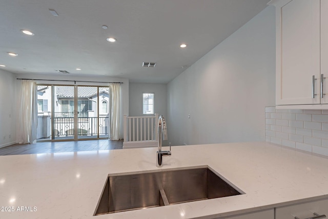 kitchen featuring light stone counters, visible vents, decorative backsplash, white cabinetry, and a sink