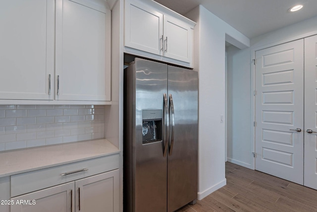 kitchen featuring tasteful backsplash, baseboards, light wood-style flooring, white cabinetry, and stainless steel refrigerator with ice dispenser