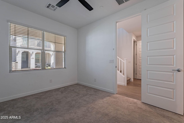 unfurnished room with baseboards, visible vents, a ceiling fan, light colored carpet, and stairs