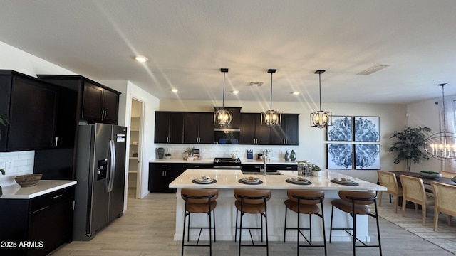 kitchen with a kitchen bar, an inviting chandelier, hanging light fixtures, a center island with sink, and stainless steel fridge