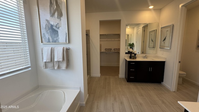 bathroom with vanity, toilet, hardwood / wood-style floors, and a tub to relax in