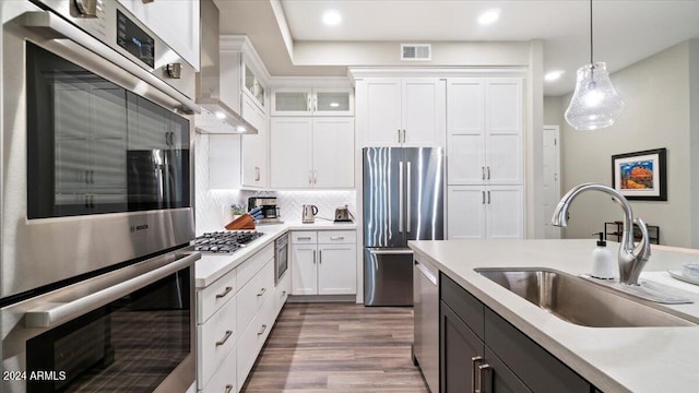 kitchen with pendant lighting, sink, hardwood / wood-style flooring, white cabinetry, and stainless steel appliances