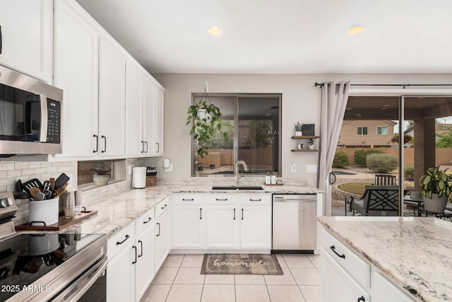 kitchen with backsplash, light tile patterned floors, white cabinets, stainless steel appliances, and a sink