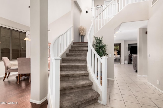 stairs featuring tile patterned flooring, a high ceiling, visible vents, and baseboards