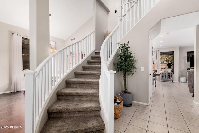 stairway featuring tile patterned floors, a high ceiling, baseboards, and visible vents