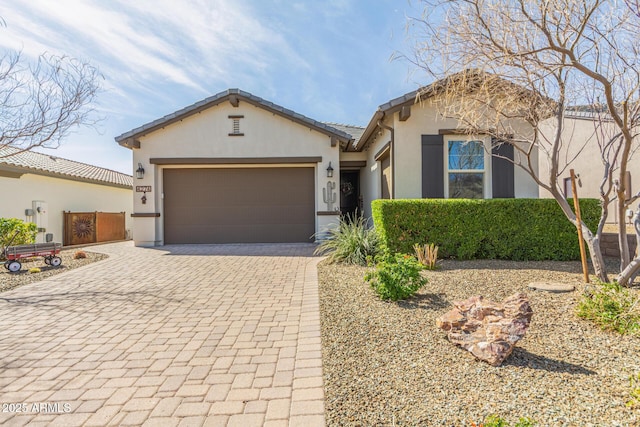 view of front facade with decorative driveway, a tiled roof, an attached garage, and stucco siding