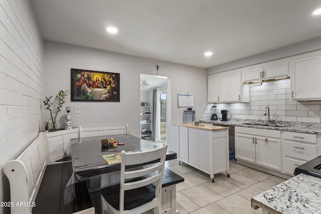 kitchen with light tile patterned flooring, white cabinetry, sink, backsplash, and light stone countertops