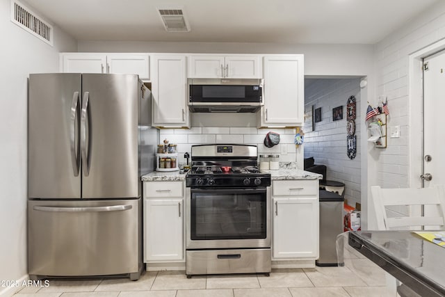 kitchen featuring stainless steel appliances, white cabinetry, light stone countertops, and light tile patterned floors