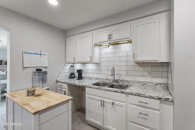 kitchen with tasteful backsplash, light stone countertops, sink, and white cabinets