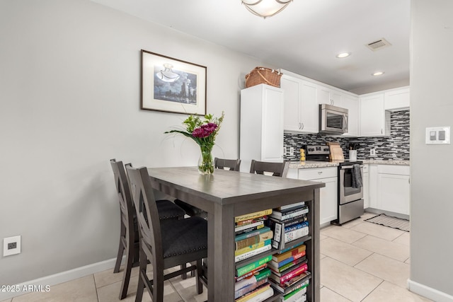 kitchen with tasteful backsplash, light tile patterned floors, stainless steel appliances, light stone countertops, and white cabinets