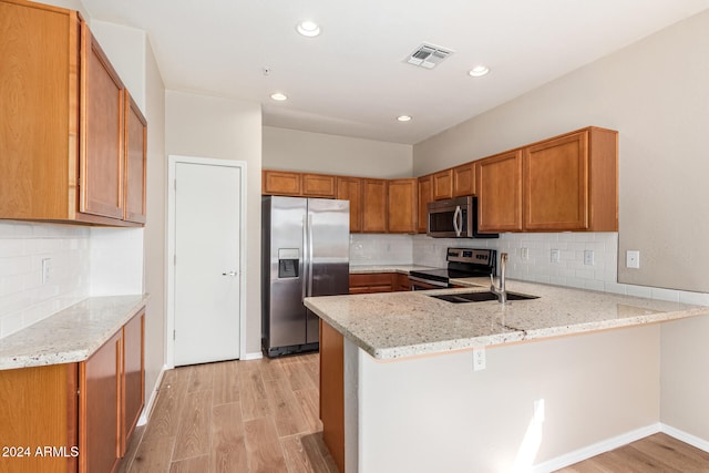 kitchen with kitchen peninsula, decorative backsplash, light stone countertops, light hardwood / wood-style flooring, and stainless steel appliances