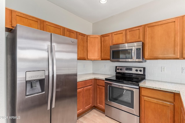 kitchen with light stone counters, appliances with stainless steel finishes, light hardwood / wood-style floors, and decorative backsplash