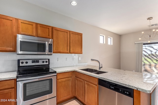 kitchen featuring kitchen peninsula, light stone counters, appliances with stainless steel finishes, sink, and decorative light fixtures