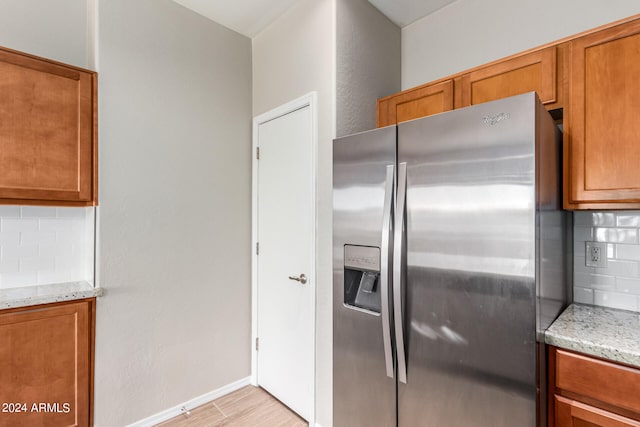 kitchen featuring light stone countertops, stainless steel refrigerator with ice dispenser, backsplash, and light hardwood / wood-style floors