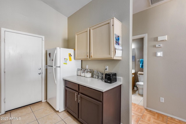 kitchen featuring dark brown cabinetry, light tile patterned floors, cream cabinetry, and white fridge