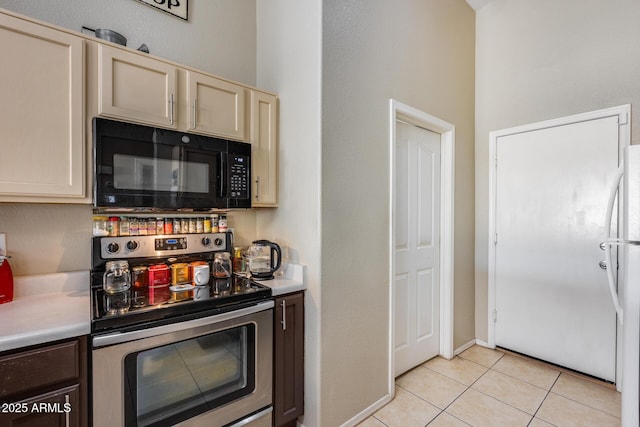 kitchen featuring cream cabinets, white fridge, light tile patterned floors, and electric range