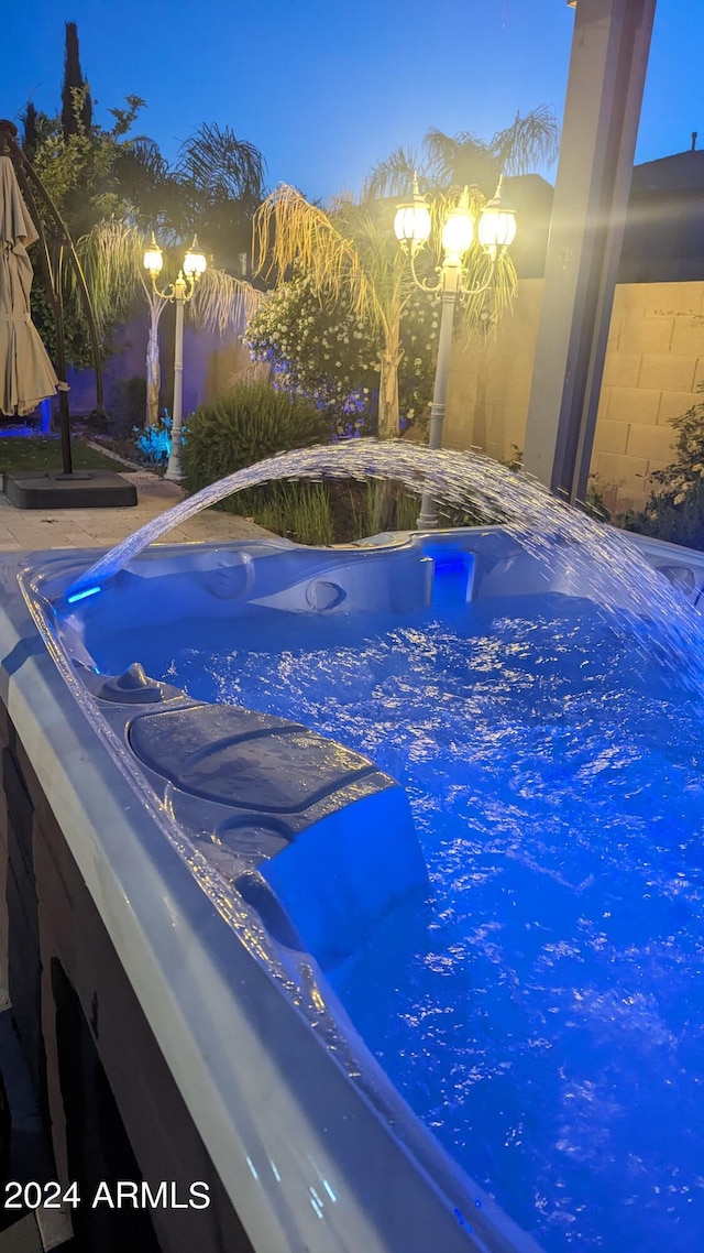 pool at dusk featuring a hot tub