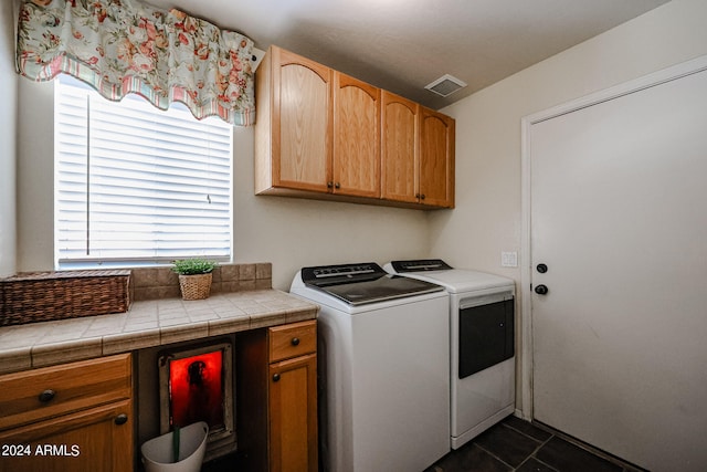 clothes washing area with dark tile patterned flooring, cabinets, and washer and dryer