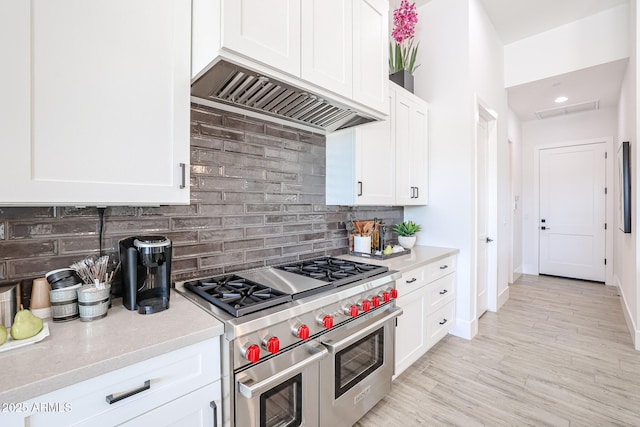 kitchen with white cabinets, decorative backsplash, double oven range, light hardwood / wood-style floors, and custom range hood