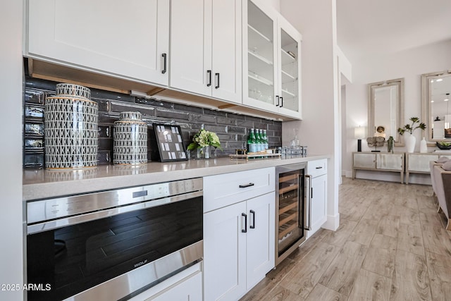 kitchen featuring white cabinetry, decorative backsplash, beverage cooler, and oven