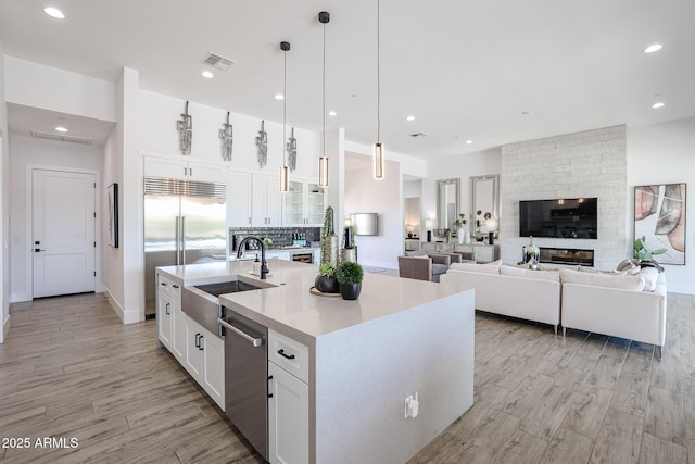 kitchen with appliances with stainless steel finishes, white cabinetry, an island with sink, sink, and hanging light fixtures