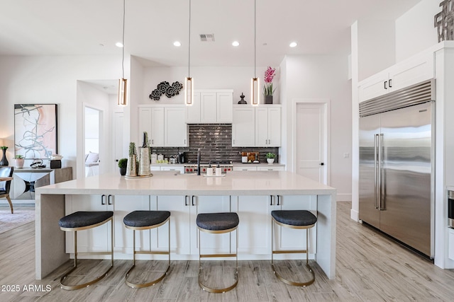 kitchen featuring decorative light fixtures, sink, an island with sink, and built in fridge