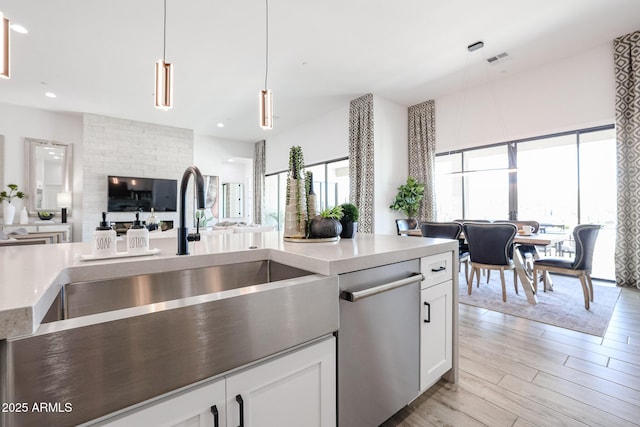 kitchen with decorative light fixtures, dishwasher, sink, and white cabinetry