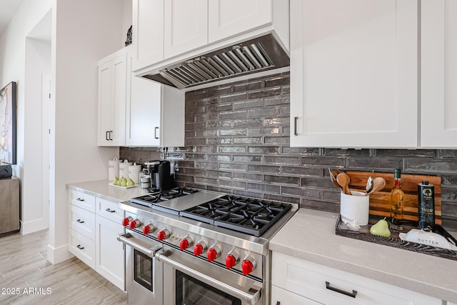 kitchen with decorative backsplash, double oven range, white cabinets, and custom range hood